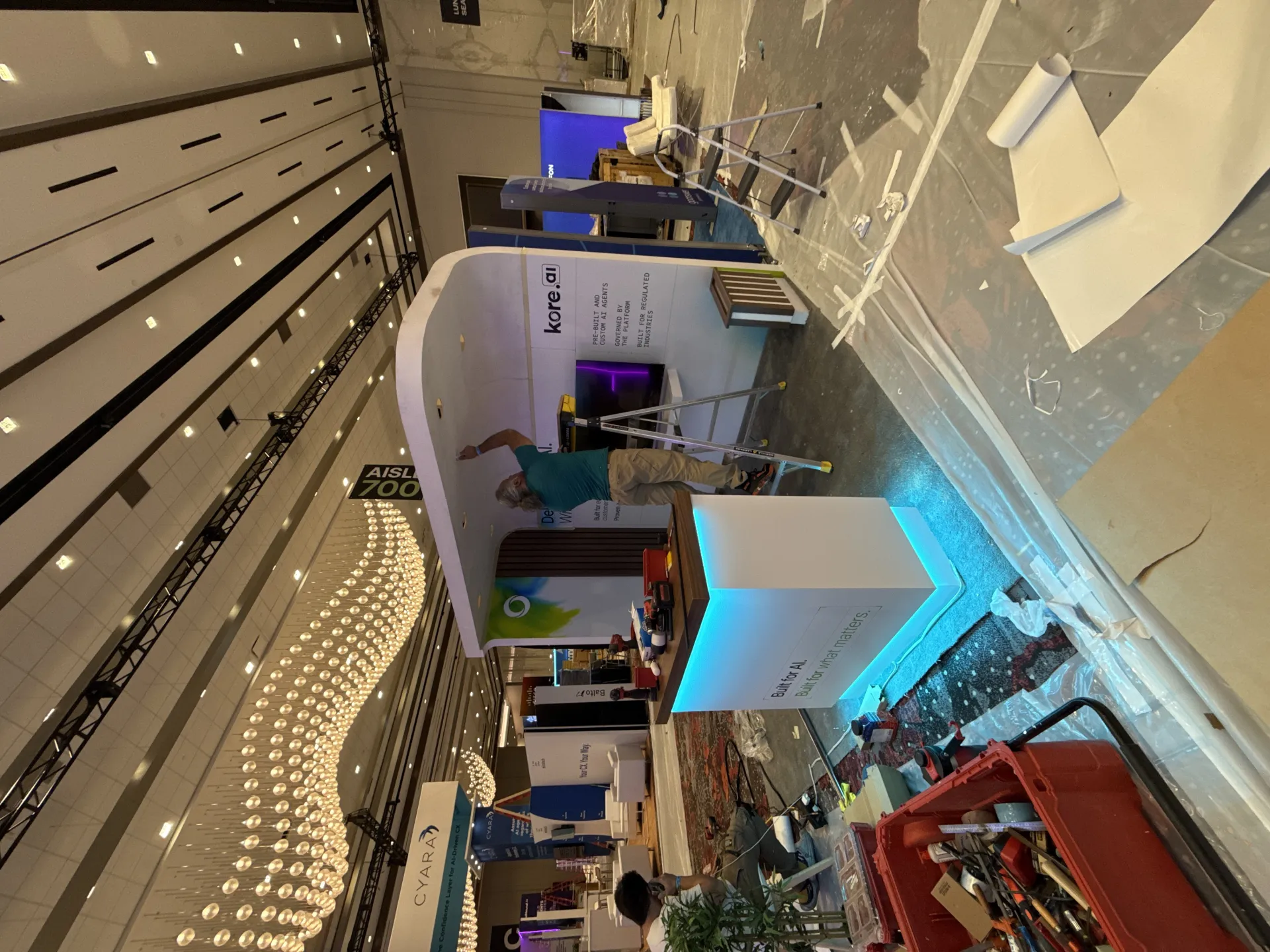 Technician on a ladder mounting the curved archway header of the kore.ai booth during install